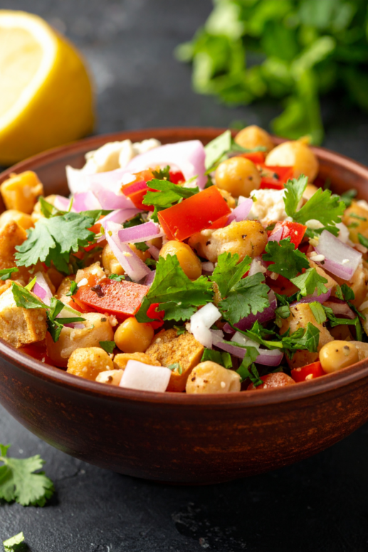 Colorful chickpea salad with diced red peppers, red onion, fresh cilantro, and lemon in a rustic wooden bowl, styled as a fresh and vibrant Mediterranean-style dish.