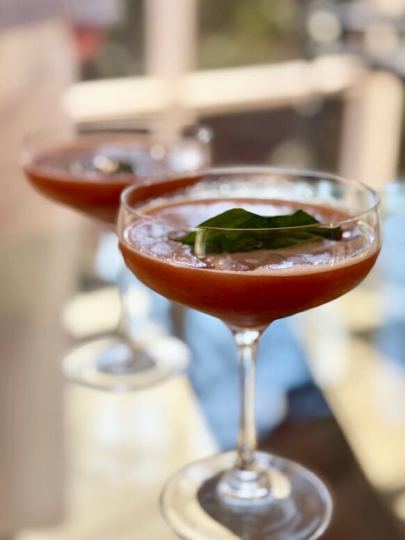 Two Strawberry Basil Smash cocktails in coupe glasses, a deep, gorgeous strawberry-red topped with fresh basil leaves, soft golden light in the background
