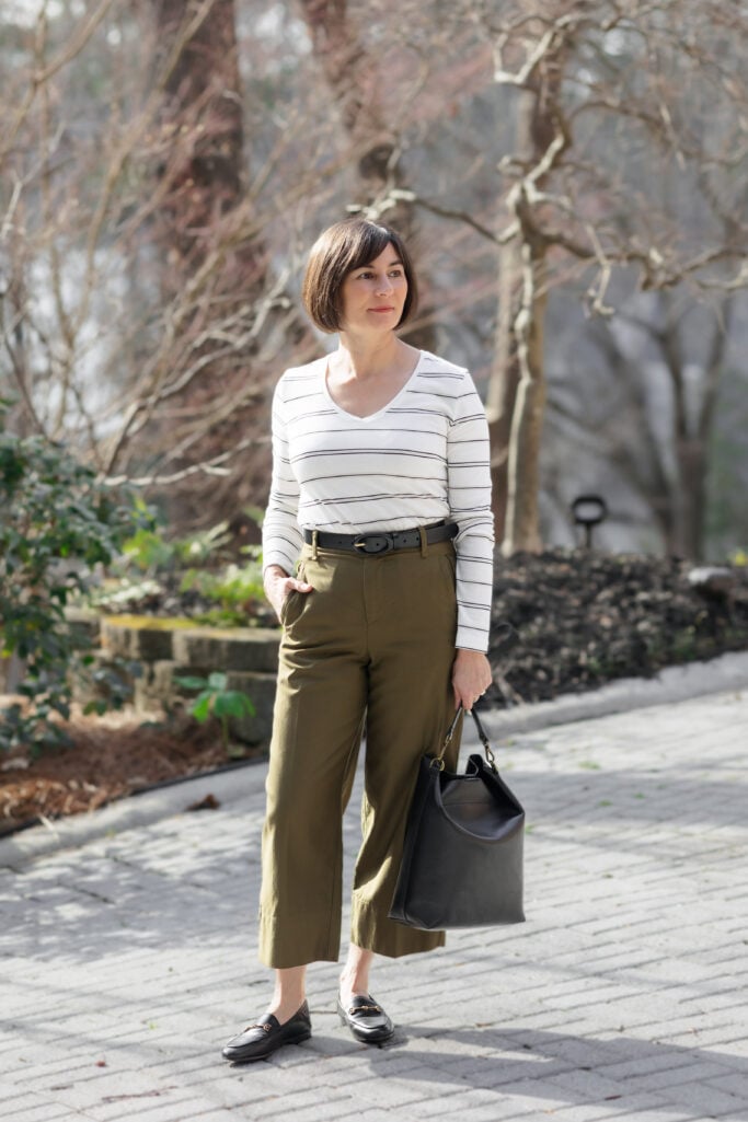Kelly looking off-camera in striped v-neck tee and green high-rise wide-leg cropped pants with black covered buckle belt, Loraine bit loafers, and Madewell bucket tote — demonstrating fitted top and wide bottom proportion for petites