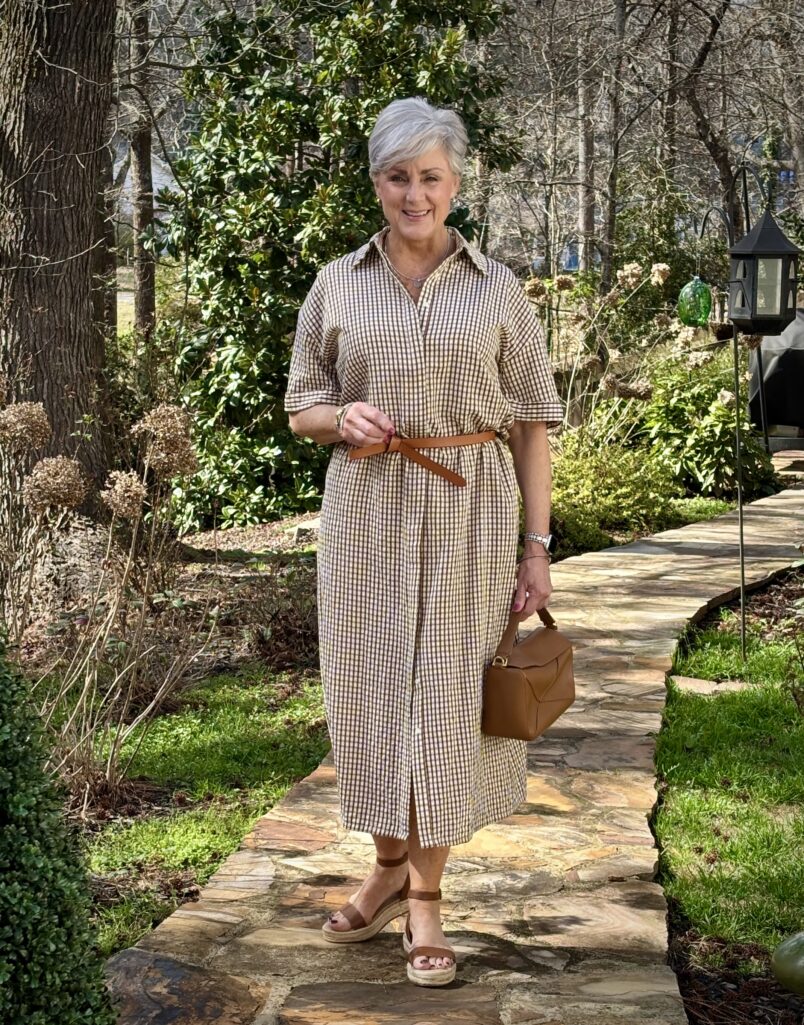 Woman over 50 wearing brown gingham midi shirtdress with cognac belt and espadrille wedge sandals — spring dresses for women over 50
