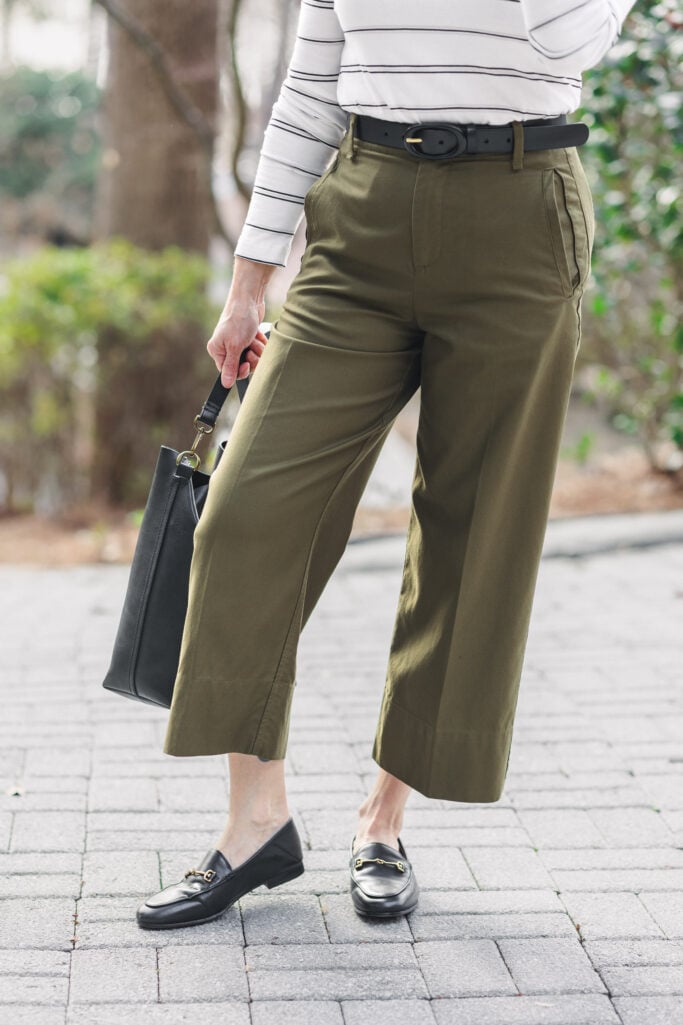 Detail shot of green wide-leg cropped twill pants with black covered buckle belt, striped tee tucked in, black Sam Edelman Loraine bit loafers, and Madewell bucket tote — showing cropped hem length and ankle gap that makes wide-leg pants work for petites