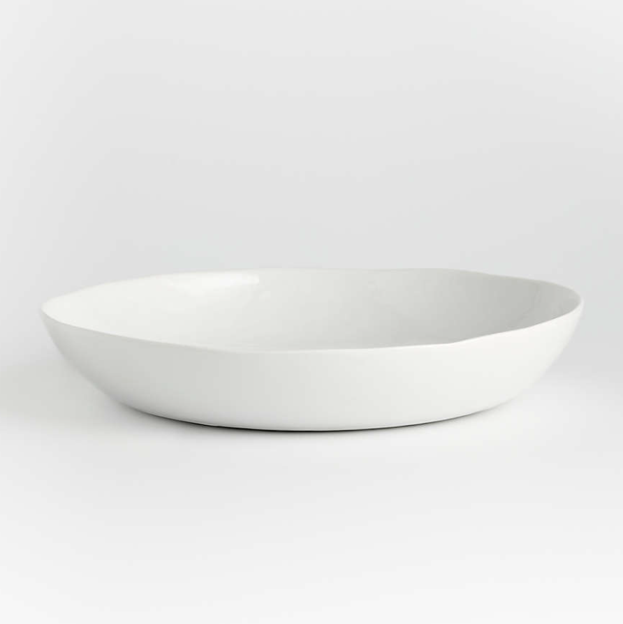 Contemporary porcelain whiteware represents a fusion of refinement and rusticity. The round slim profile of this serving bowl takes on organic overtones with freeform rims and a finely "hammered" surface that ripples the light. Smooth enough to not harm tables, the unglazed ceramic bottom gives each piece an artisanal look.