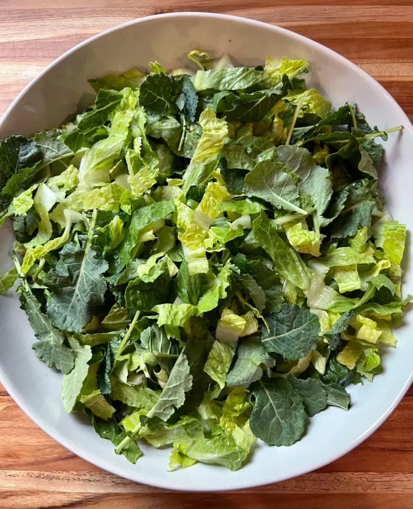 Overhead view of chopped romaine lettuce and baby kale in a wide white serving bowl