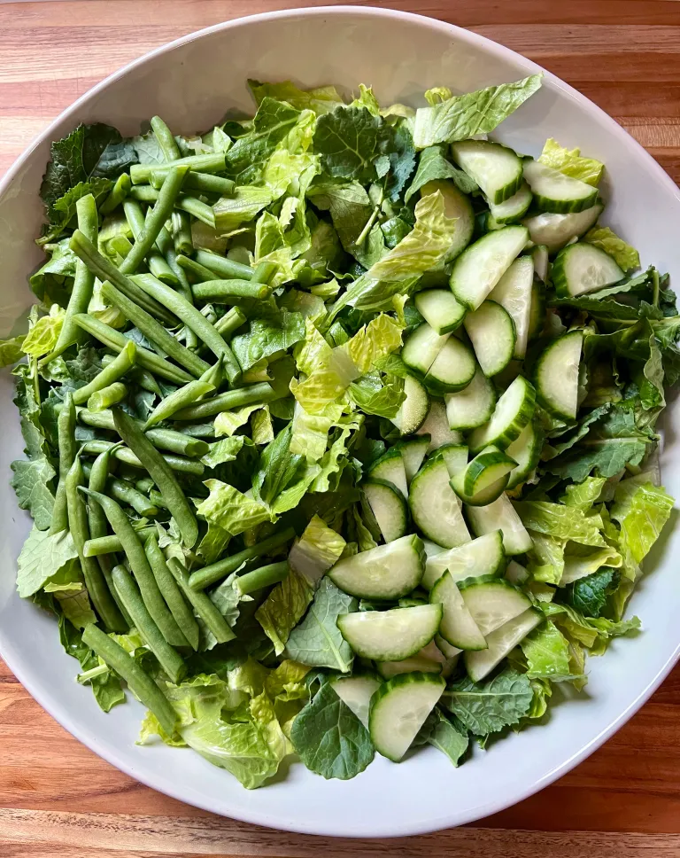 Overhead view of green beans and sliced cucumbers arranged in columns on the bed of lettuce