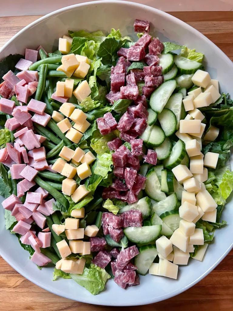 Overhead view of diced sharp white cheddar and smoked Gouda added in columns alongside the meats and vegetables