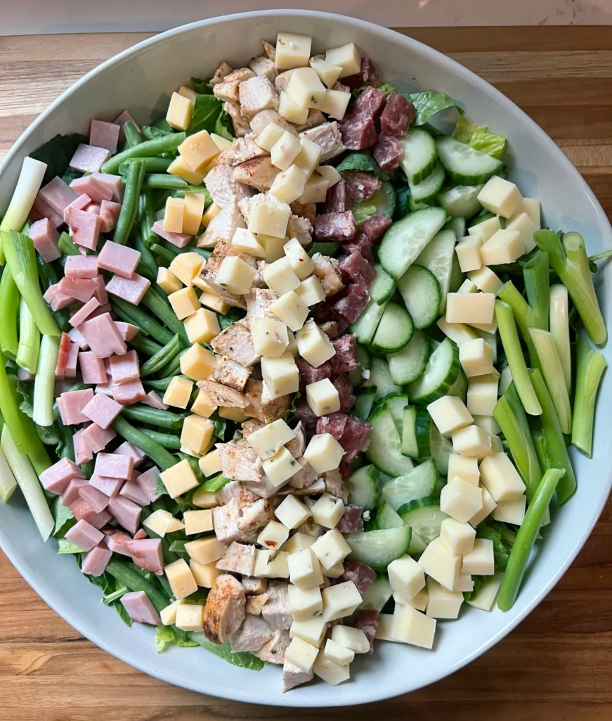 Overhead view of diced chicken breast, cubed pepper jack cheese, and scallion strips added to complete the salad assembly