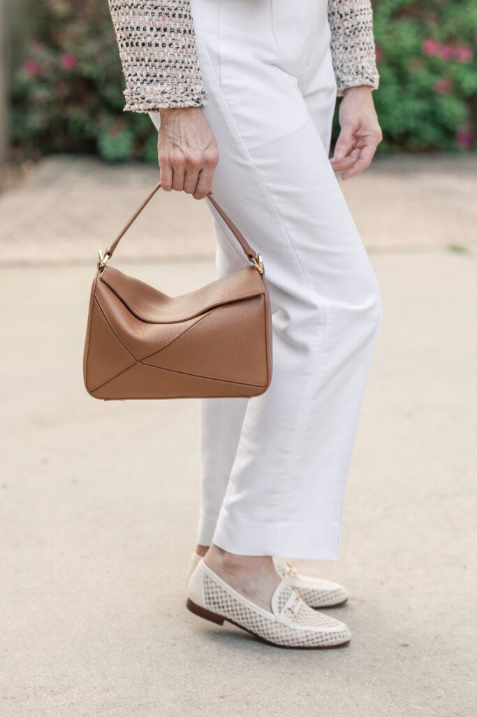 Close-up of Quince Italian leather patchwork bag in cognac held with white straight-leg trousers and cream mesh loafers — spring bag for petite outfit