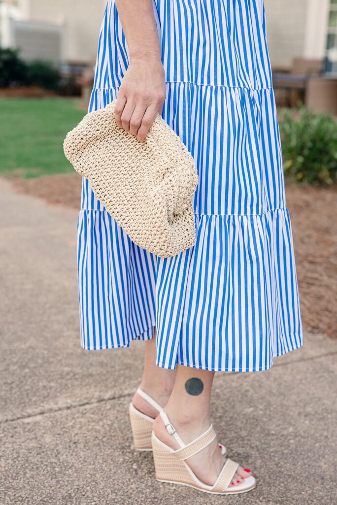 Close-up of Portofino handknotted straw clutch and nude wedge sandal against blue and white striped tiered dress hem — summer accessories for petite occasion dress
