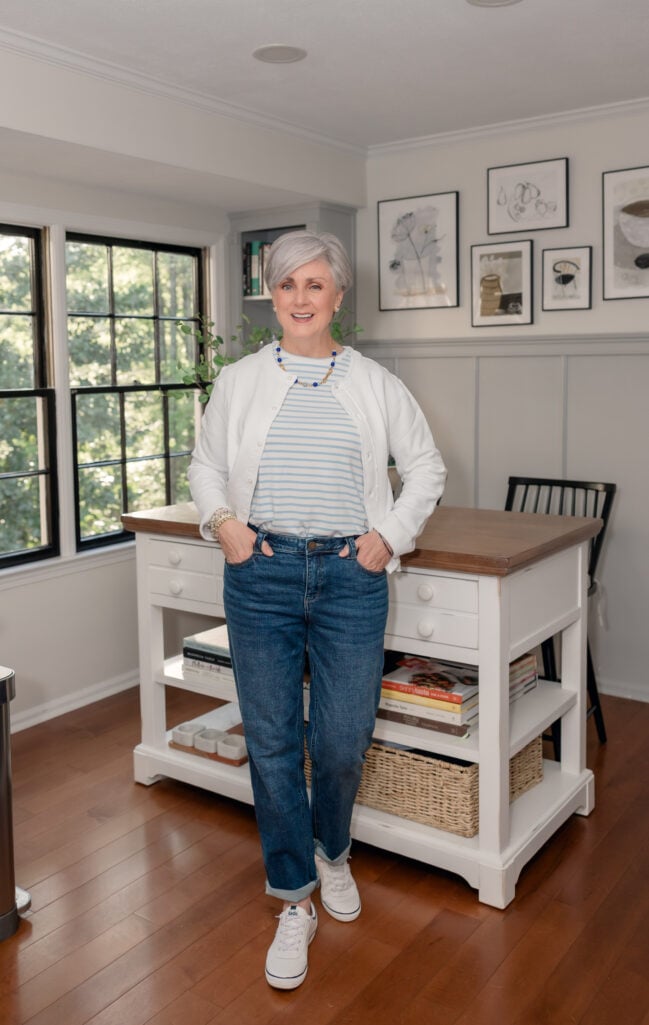 how to develop personal style after 50 — woman in a relaxed everyday outfit of striped tee, white cardigan, and cuffed jeans at home, illustrating wardrobe basics that work