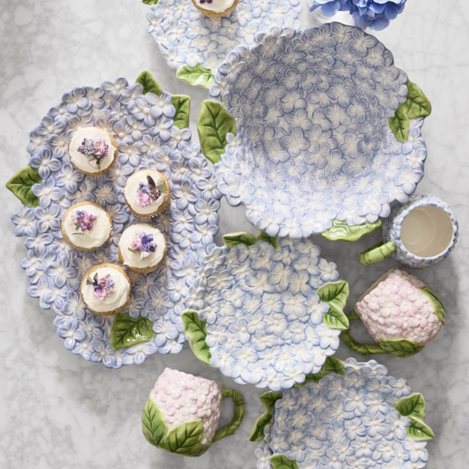 Williams Sonoma Hydrangea Dinnerware Collection featuring blue hydrangea-inspired plates, serving bowls, mugs, and platters with hand-painted floral petals and green leaf accents on stoneware.