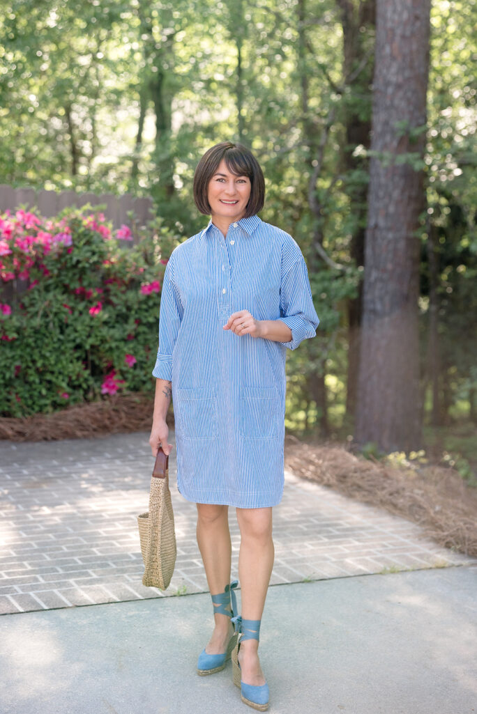Kelly in full-length blue striped broadcloth shirtdress with blue Castañer espadrille wedges and straw hobo bag, hand in patch pocket — petite shirtdress styling