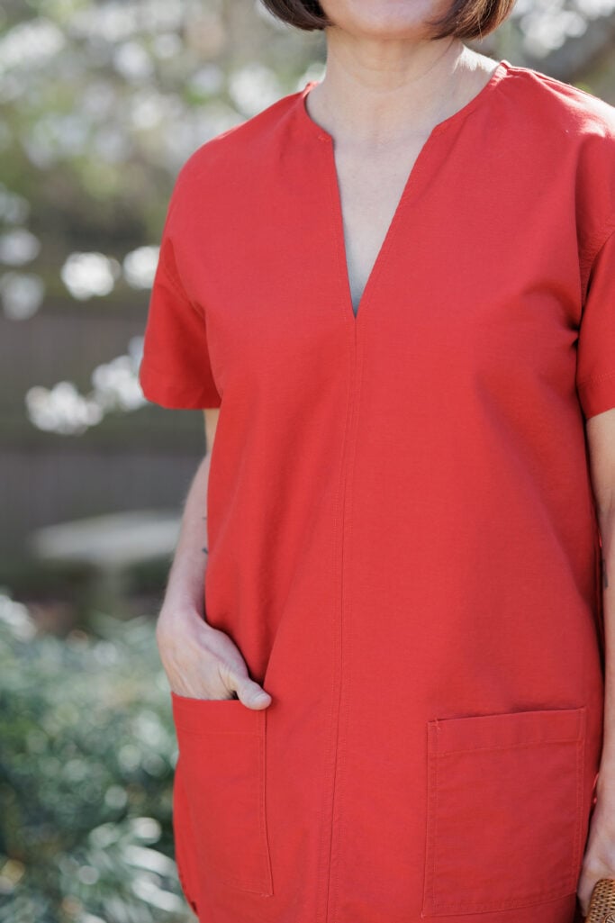 Close-up of red pullover dress showing V-neckline seam detail and front patch pockets, hand in pocket — petite-friendly dress features for spring