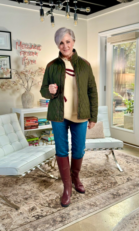 Woman wearing a quilted green jacket, cream sweater, jeans, and tall brown riding boots, styled in a cozy, modern living room.
