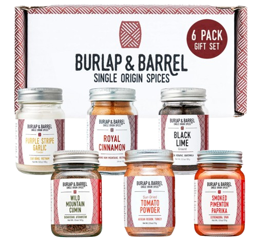 Six glass spice jars with metal lids in a gift box, labeled varieties including royal cinnamon, black lime, wild mountain cumin, and smoked paprika.