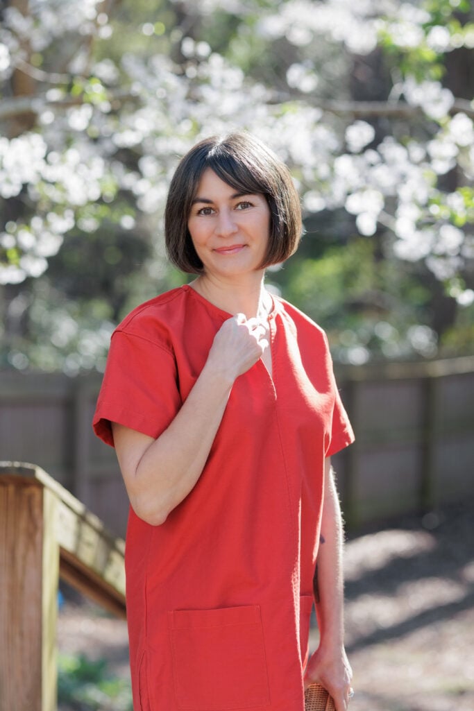 Kelly in red pullover dress, portrait shot with soft-focus spring cherry blossoms — red shift dress petite women