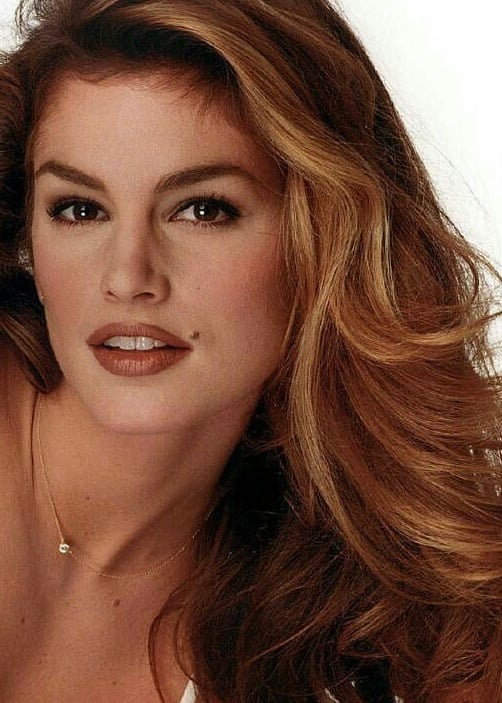 Vintage 90s beauty portrait of supermodel with long voluminous highlighted brown waves, matte bronzed skin, soft smoky brown eyes, warm nude-brown lips, and delicate diamond pendant necklace