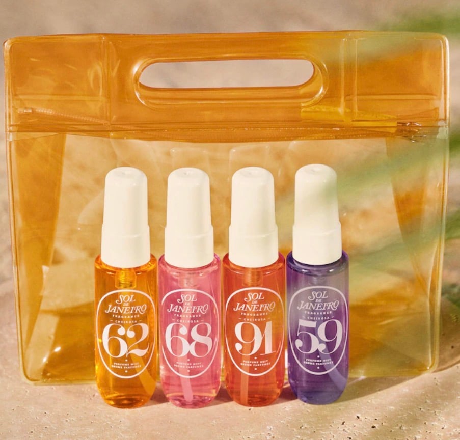 Product flat lay of Sol de Janeiro Cheirosa Perfume Mist Discovery Gift Set showing four travel-size fragrance mist bottles numbered 62, 68, 91, and 59 in amber, pink, coral and purple, displayed in front of yellow translucent jelly clear zip pouch bag on sandy neutral background