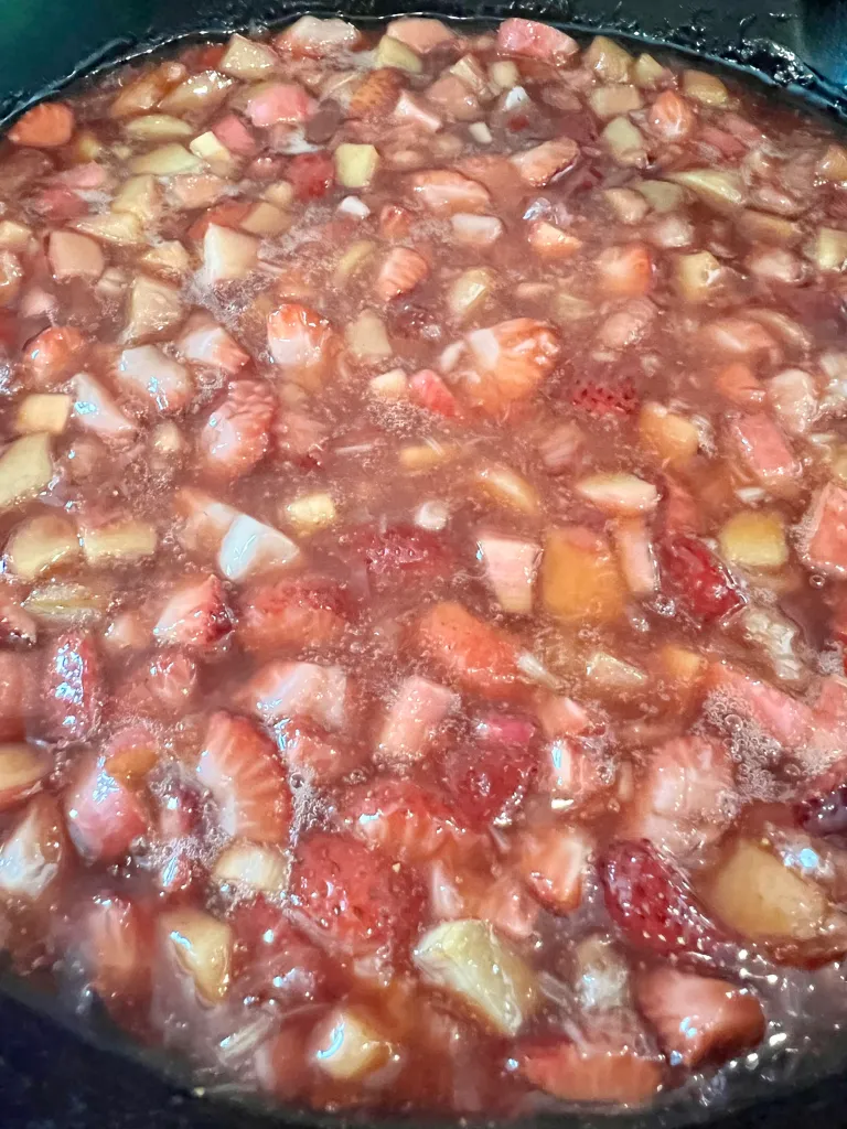 Fully cooked strawberry-rhubarb filling in a cast iron skillet, with the bright red jammy liquid nearly covering the softened fruit