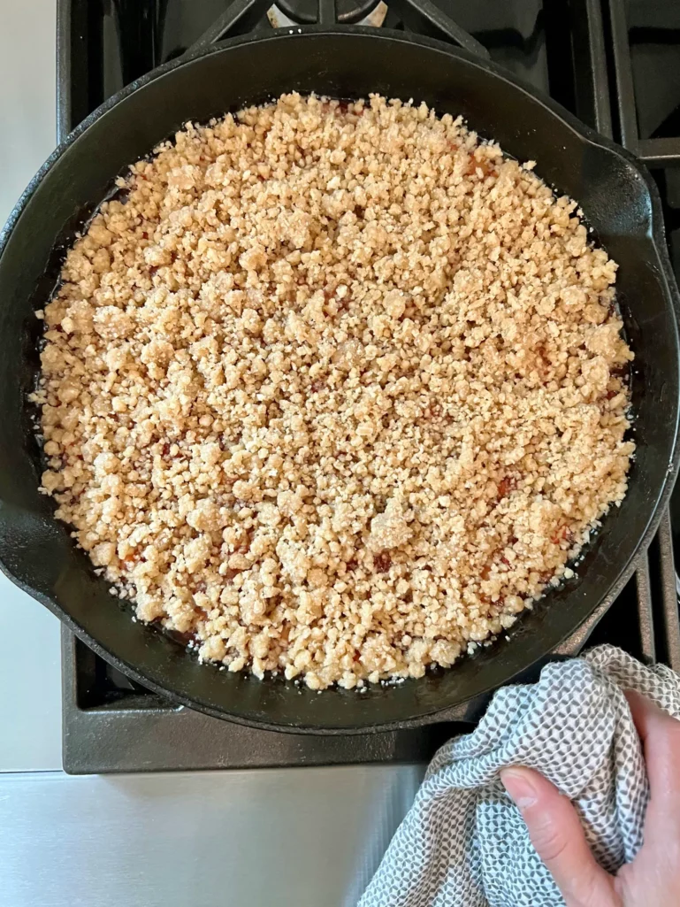 Overhead view of the cast iron skillet fully topped with the panko crisp topping, ready to go into the oven, held with a kitchen towel