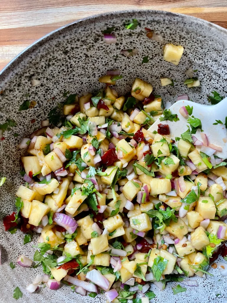 Finished chipotle pineapple salsa mixed together in a speckled ceramic bowl, showing diced pineapple, red onion, cilantro, and chipotle peppers in adobo