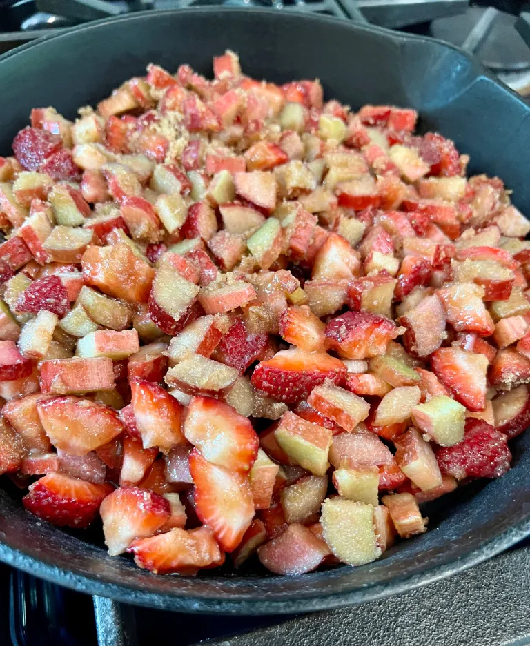 Strawberry-rhubarb filling with sugar and cornstarch transferred to a cast iron skillet, ready to cook on the stovetop