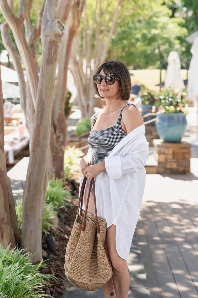 Kelly in black gingham J.Crew square-neck one-piece swimsuit with white linen beach shirt slipped off one shoulder, oversized sunglasses, and raffia tote — petite swimwear styling