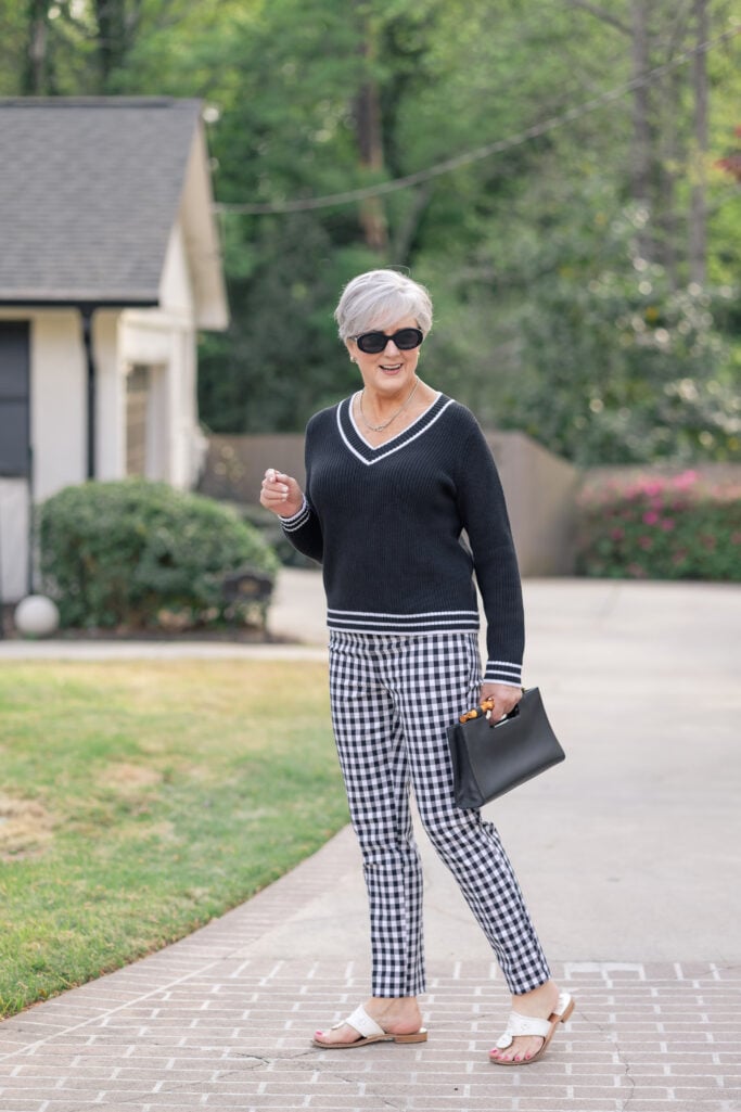 Black V-neck tipped sweater with black-and-white gingham pants and Jack Rogers sandals — classic neutral anchor outfit for styling bold color after 50
