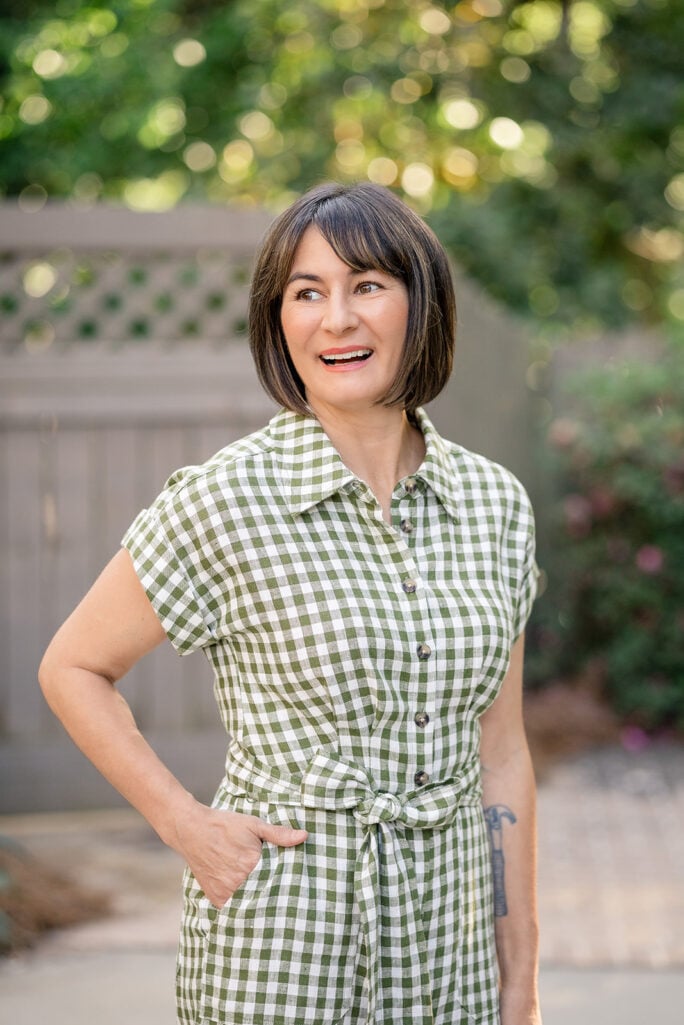 Kelly smiling in olive gingham linen romper with cap sleeves, tie waist, and button-up bodice — petite playsuit summer styling