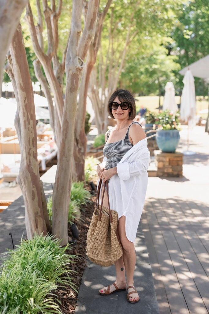 Kelly in white linen button-front beach shirt over black gingham square-neck swimsuit with raffia tote — petite swimwear cover-up styling
