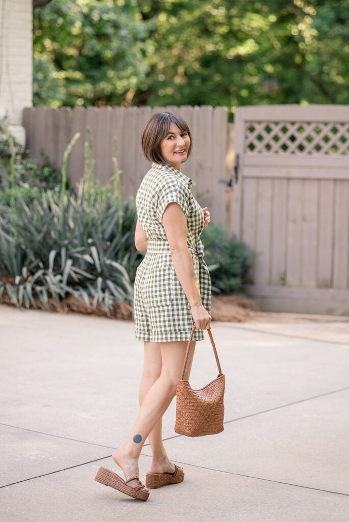 Back view of Kelly in olive gingham linen romper with tie waist showing cap sleeve and shorts proportions — petite playsuit styling