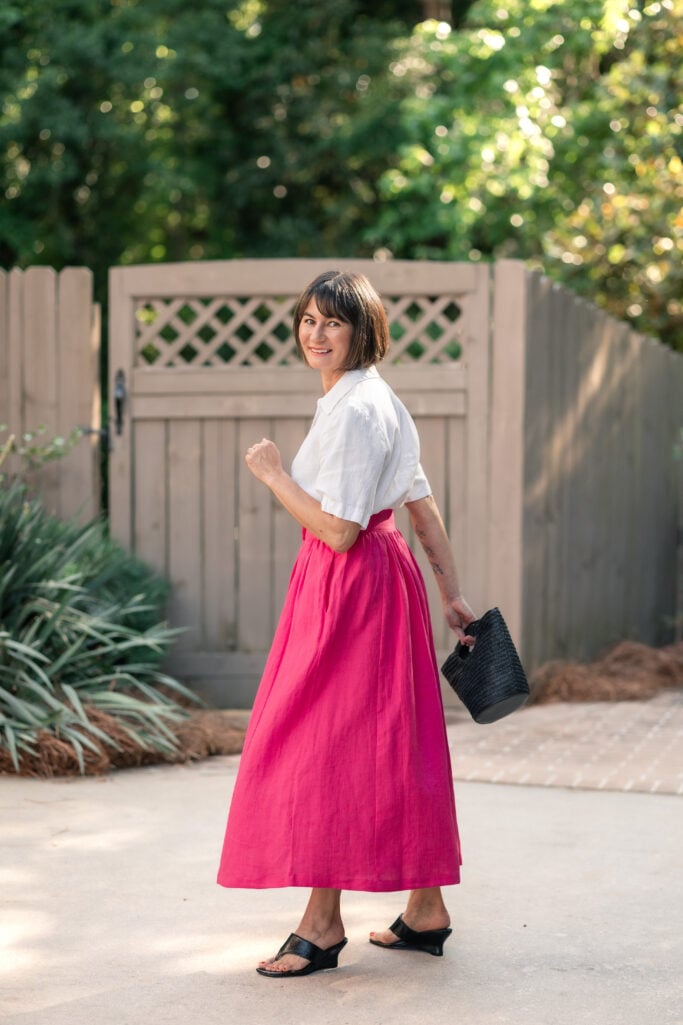 Kelly turning over shoulder in white linen popover and hot pink linen maxi skirt with black straw bag — petite summer separates in motion