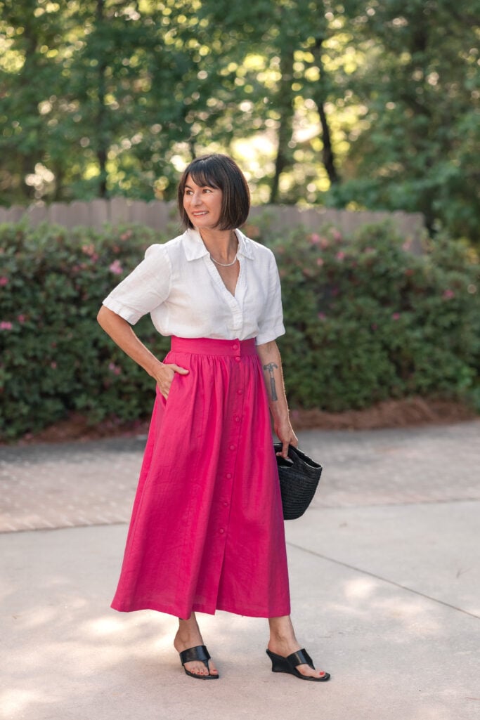 Kelly with hand in pocket of hot pink Boden Emma linen maxi skirt styled with tucked white linen popover and black wedge sandals — petite summer separates formula