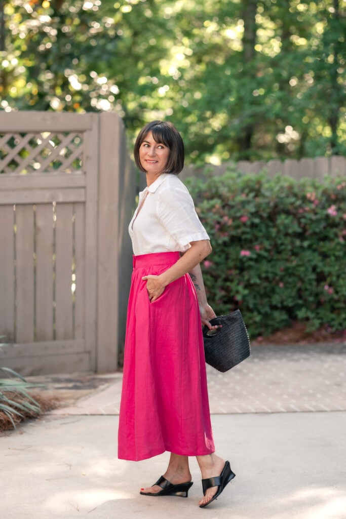 Side-back view of Kelly in tucked white linen popover and hot pink linen maxi skirt with black straw mini bucket bag — petite maxi skirt styling