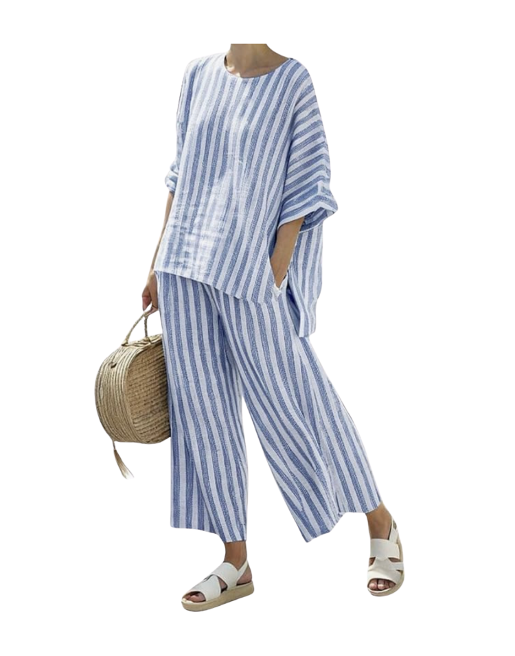 Two-piece blue and white vertical-stripe linen lounge set featuring a relaxed oversized long-sleeve crewneck top and matching wide-leg pull-on pants, styled with white woven sandals and a round straw handbag — a coordinated linen lounge set for summer mornings and evenings.