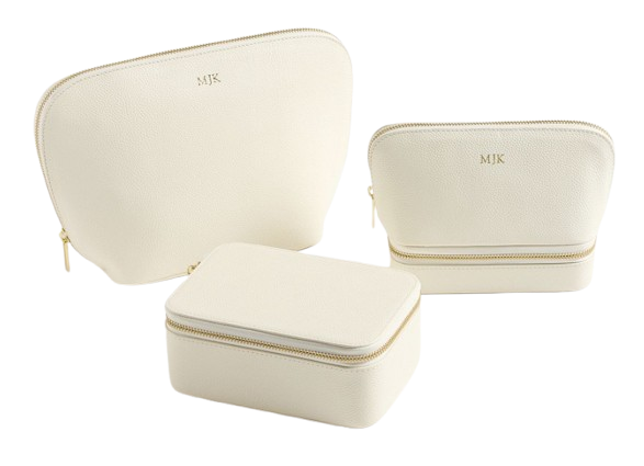 Set of three cream leather travel pouches with gold zippers and monogram initials, in large, medium, and rectangular shapes for makeup and accessories.