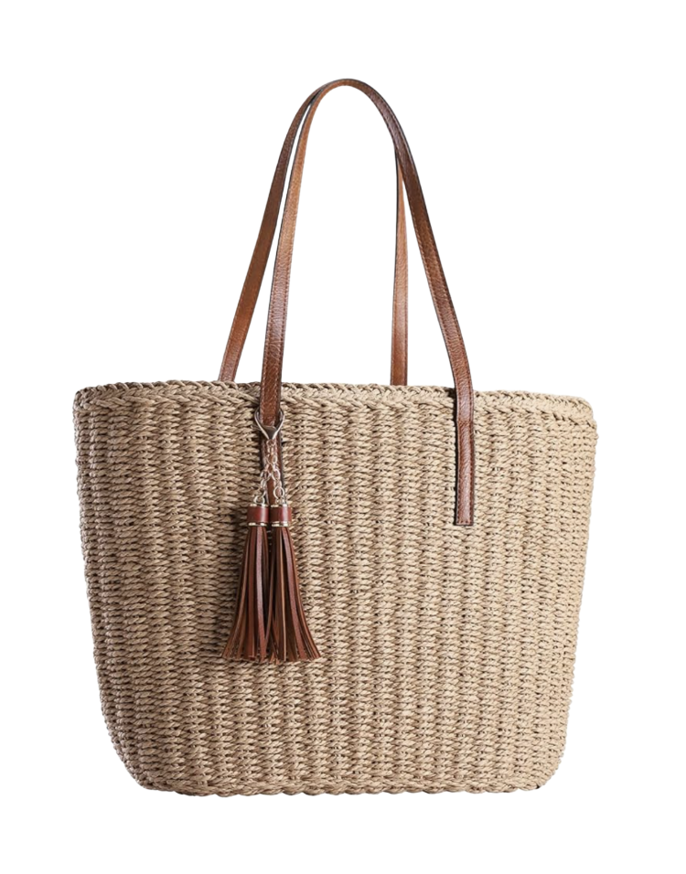 Natural woven straw tote bag with long cognac leather shoulder straps and a leather tassel charm — a structured straw summer tote bag for beach, brunch, and farmers' market.