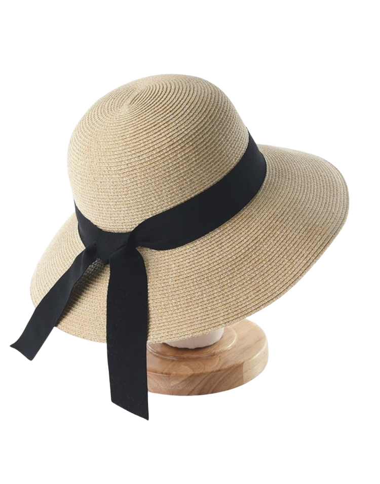 Natural straw wide-brim sun hat with a long black grosgrain ribbon band tied in a bow, displayed on a wooden hat stand — a packable wide-brim summer sun hat for women over 50.