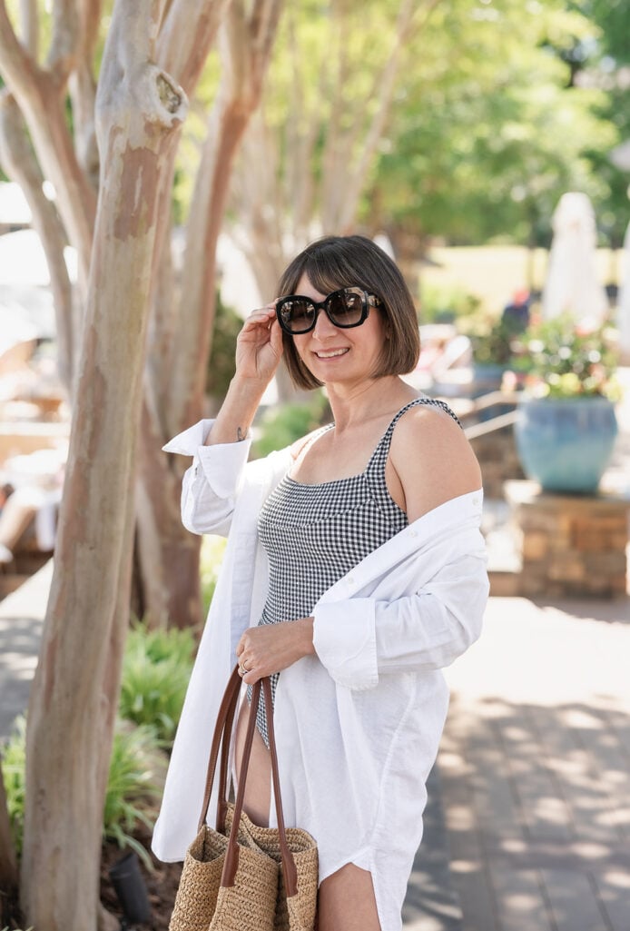 Close-up portrait of Kelly in oversized Prada tortoise sunglasses with white linen beach shirt and black gingham swimsuit — petite resort accessories