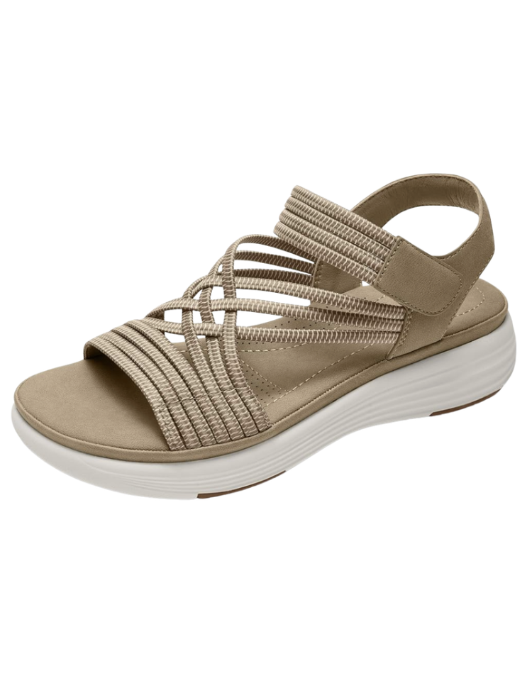 Tan strappy comfort walking sandal with woven elastic straps, cushioned suede footbed, adjustable hook-and-loop closure at the heel, and a white rubber sole — a supportive all-day walkable summer sandal for women over 50.