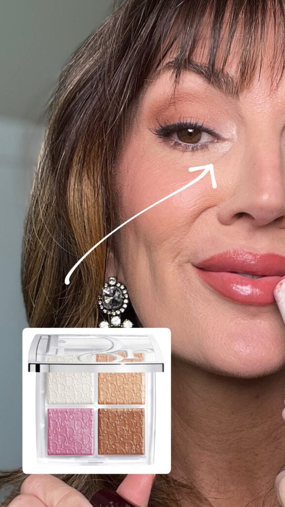 Close-up of finished eye makeup with arrow pointing to bright white inner corner highlight, showing curled lashes with mascara, soft smoky brown shadow, and glossy nude rose lips, with Dior Backstage Glow Face Palette in white pink and bronze shades displayed below