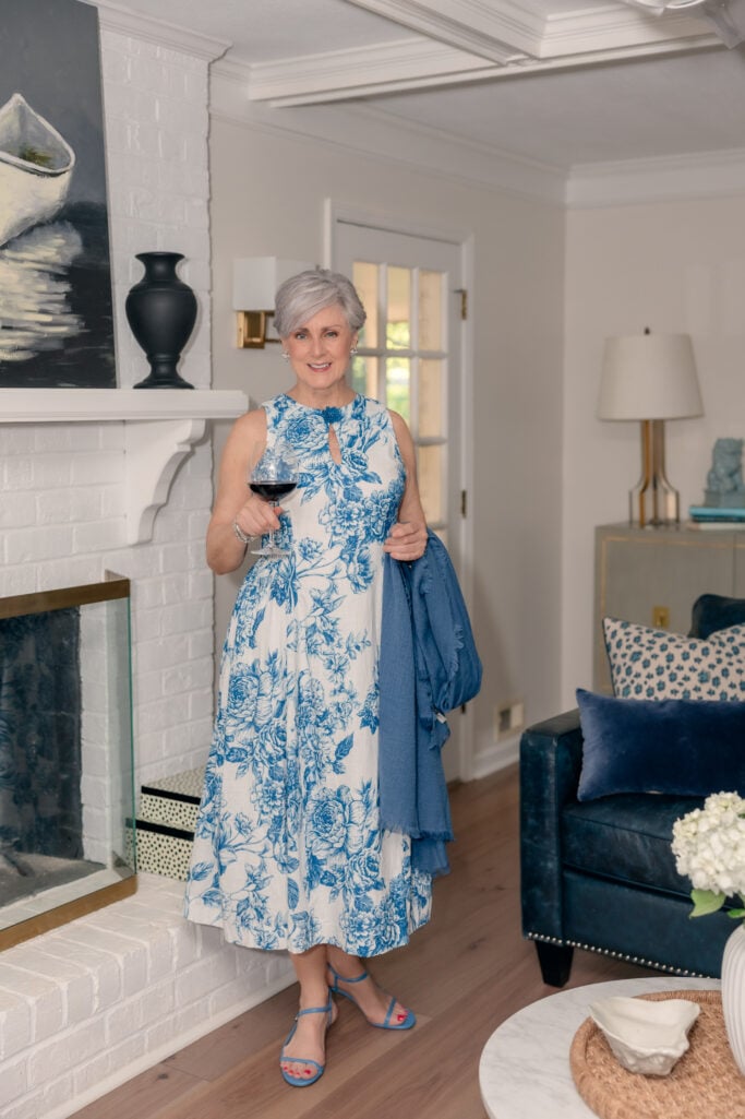 Woman over 50 wearing a blue and white floral dress with a wrap and strappy sandals for a summer wedding.