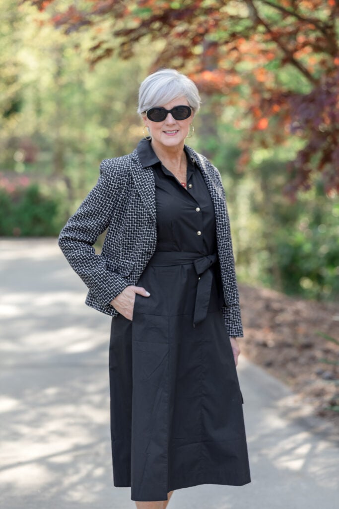 Beth wearing a solid black poplin shirtdress belted under a black and white tweed blazer