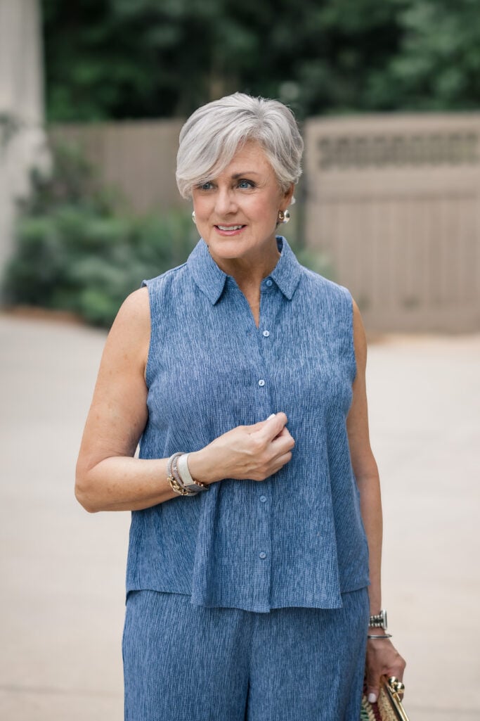Woman over 50 with silver hair in a sleeveless blue crinkle-texture button-up top and matching wide-leg pants from Eileen Fisher