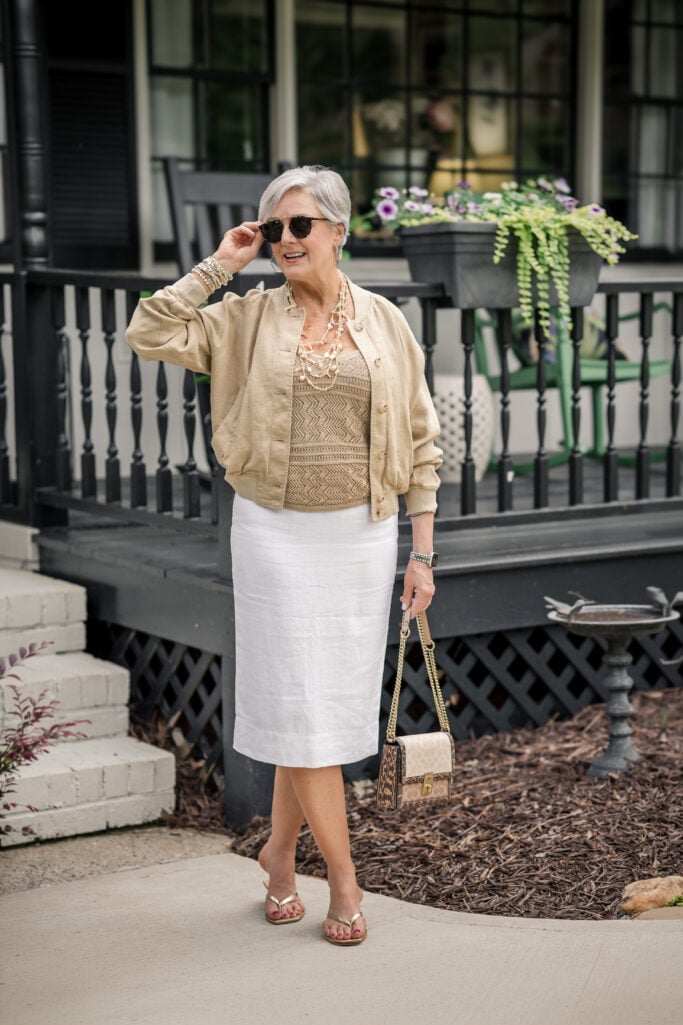 Weekend travel outfit over 50 dressed up — linen bomber jacket, white linen midi skirt, and gold sandals.