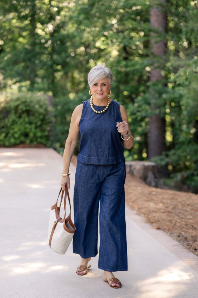 Woman over 50 wearing a polished summer denim outfit with leather sandals and a canvas tote
