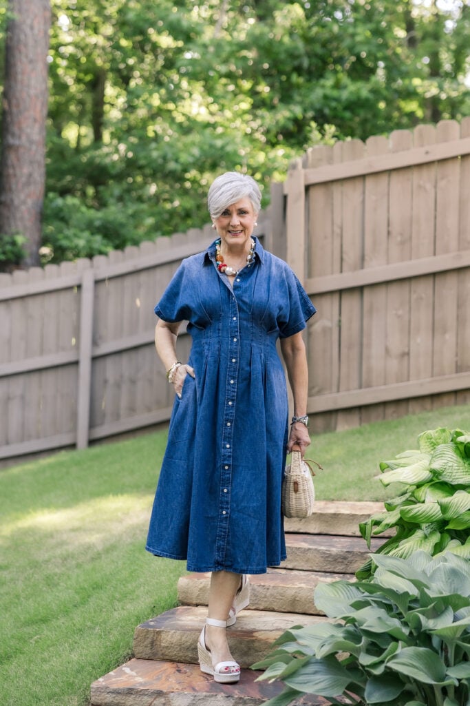 Denim shirtdress outfit for women over 50 styled with espadrille wedges, beaded necklace and woven handbag