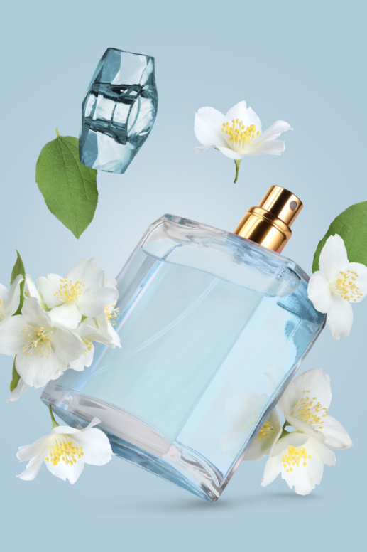 Light blue perfume bottle surrounded by delicate white jasmine blossoms and green leaves against a soft blue background, creating a fresh, airy fragrance-inspired beauty flat lay.