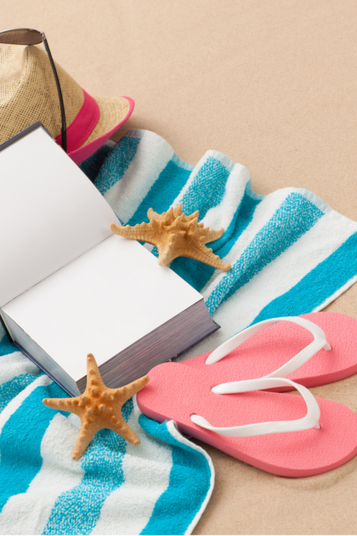 Beach towel with turquoise and white stripes laid on the sand, styled with pink flip-flops, an open book, a straw sun hat, sunglasses, and starfish for a relaxing summer beach scene.