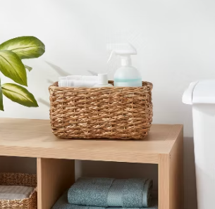 Rectangular woven seagrass storage basket with built-in handles, styled on a shelving unit and designed for organizing toiletries, linens, or household essentials.