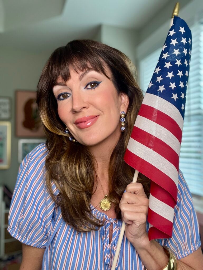 Woman holding a small American flag indoors wearing elegant 4th of July makeup